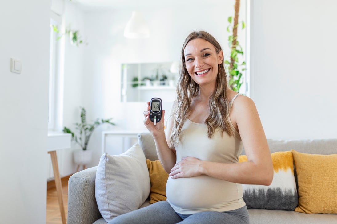 Happy Pregnant woman with glucometer checking blood sugar level at home. Woman testing for high blood sugar. Pregnant Woman holding device for measuring blood sugar